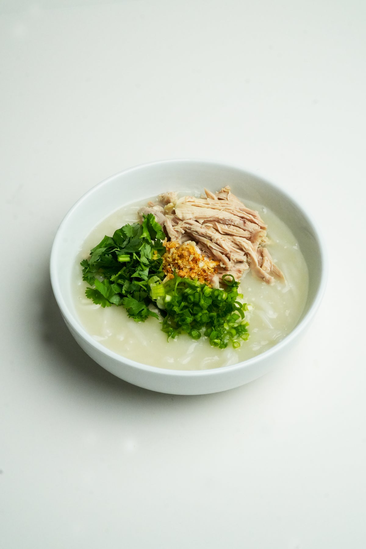 Bowl of Khao Piak Sen Lao chicken noodle soup made with Dog Dig fresh rice noodles, topped with chicken, fried garlic and green onion